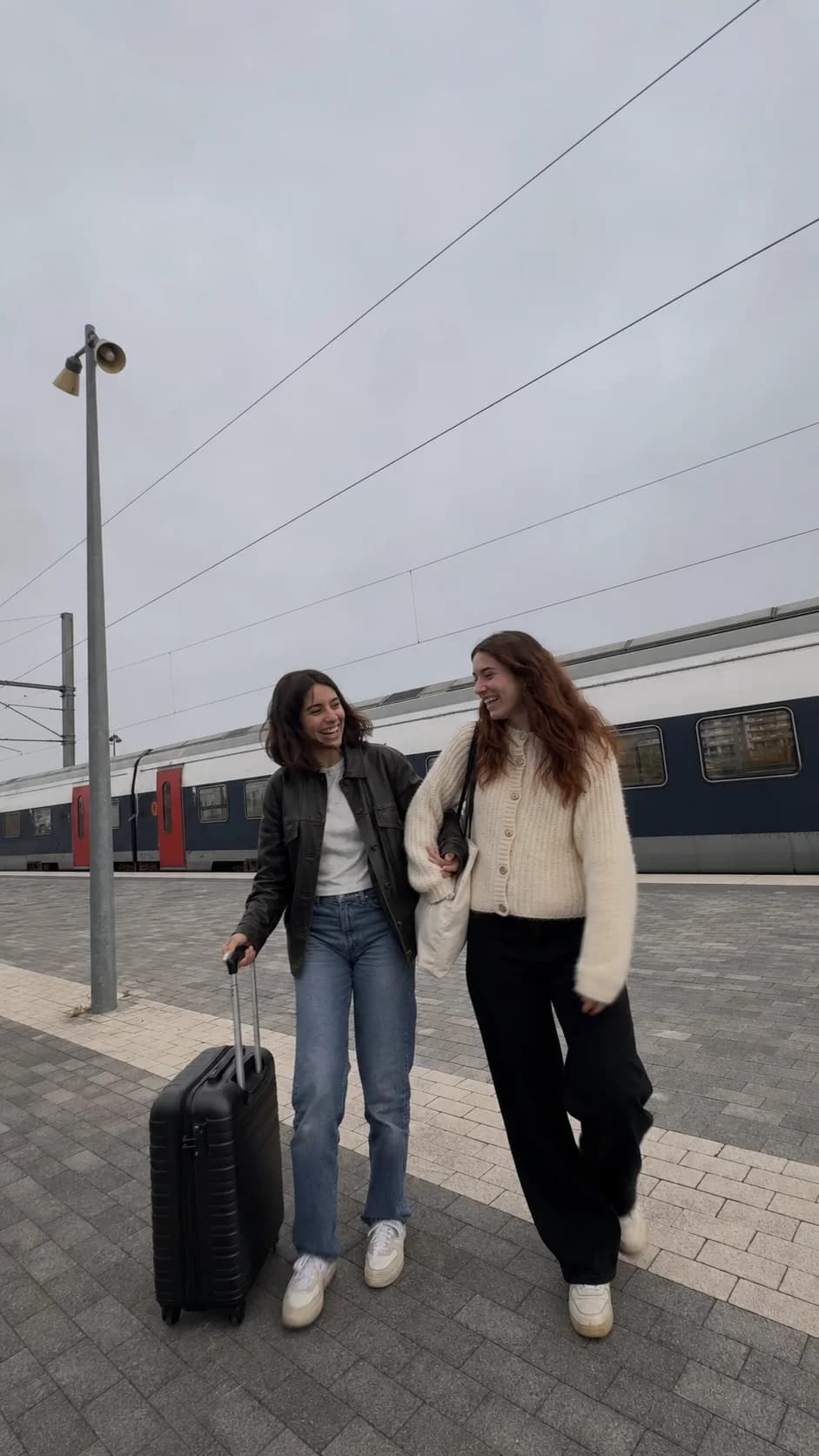 Two friends laughing together on an early-morning train platform