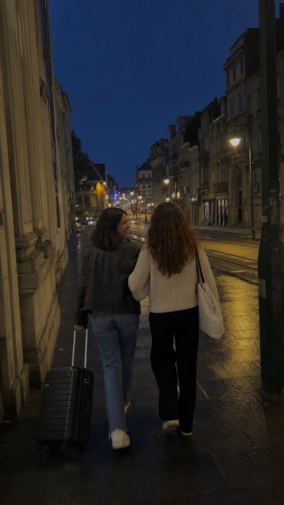 The friends walking arm in arm down a wet street at night
